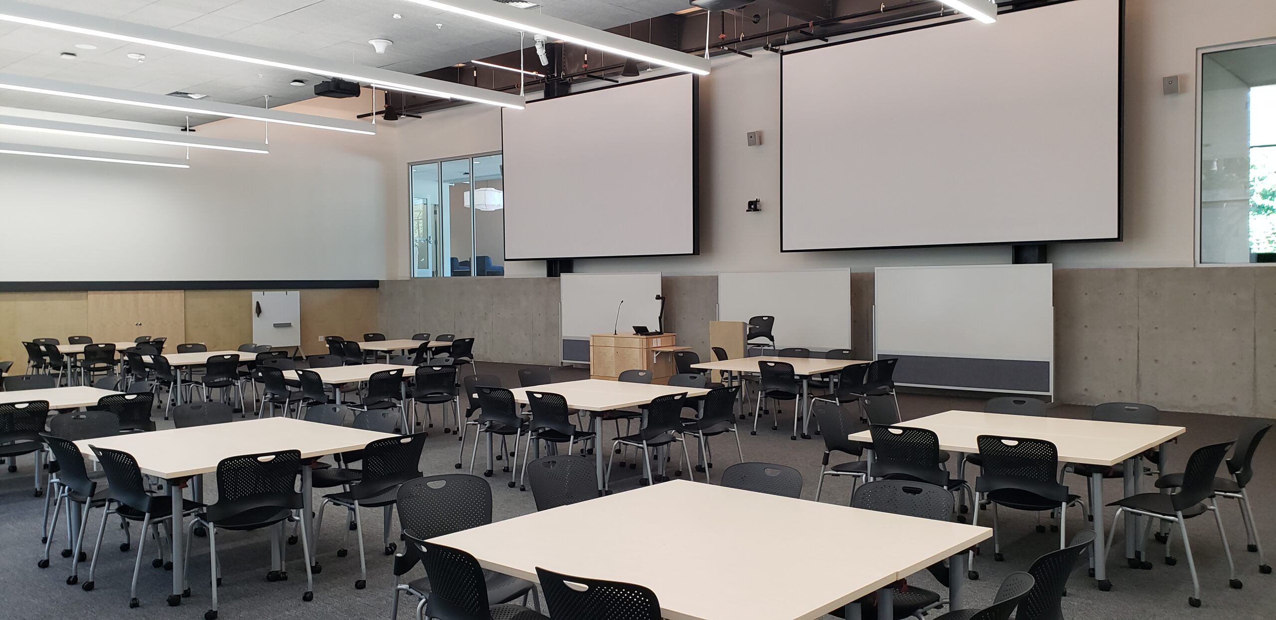 A photo of the HSEB 101 classroom taken from the back right corner, showing the presenter’s podium and projectors.