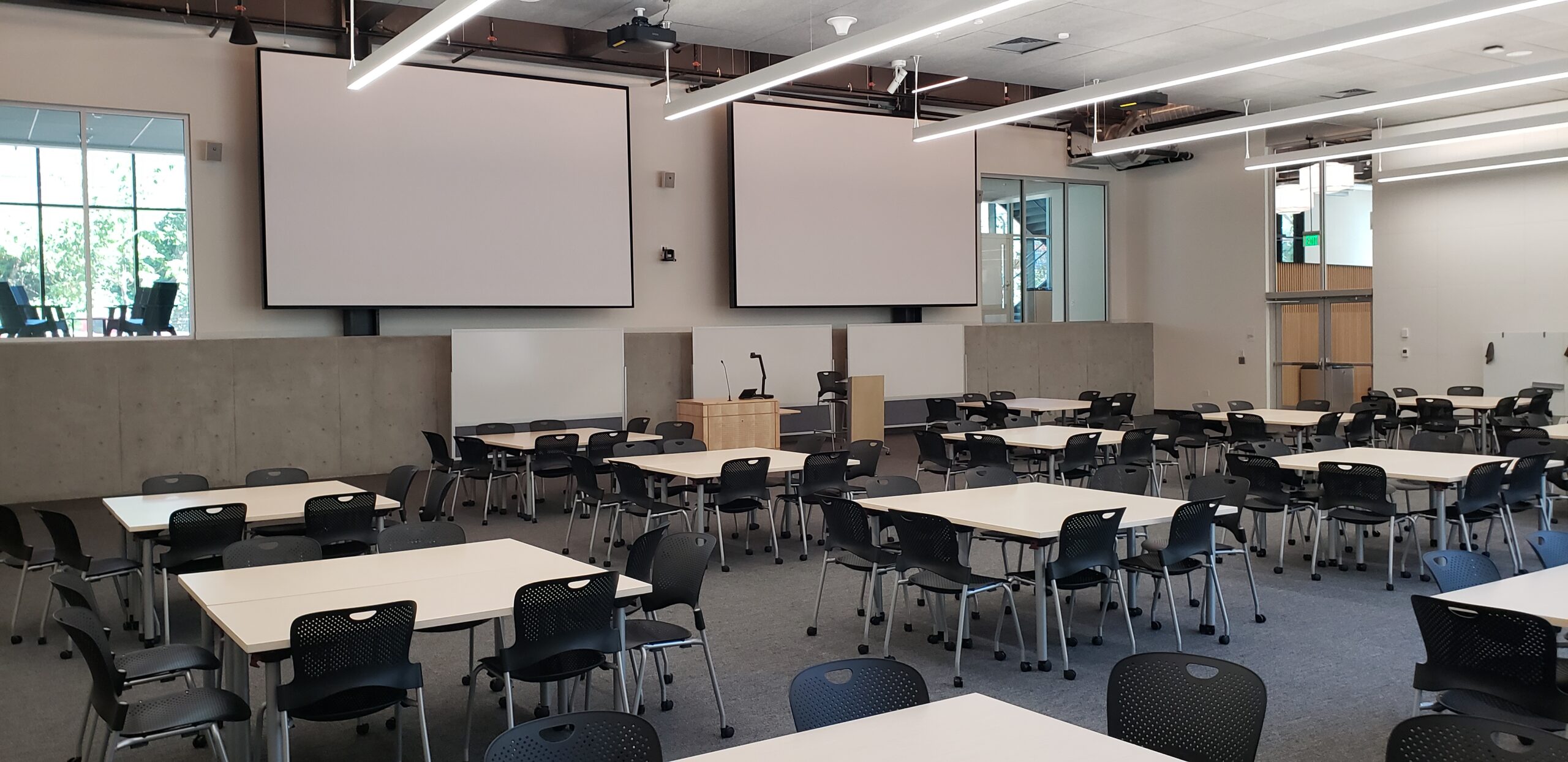 A photo of the HSEB 101 classroom taken from the back left corner, showing the presenter’s podium and projectors.