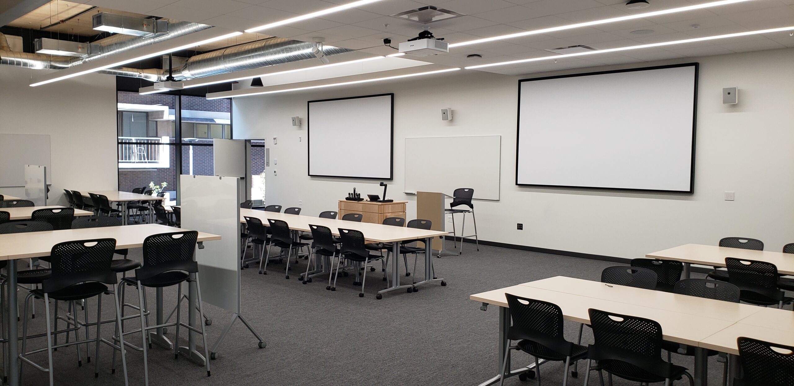 A photo of the HSEB 125 classroom taken from the back right corner, showing the presenter’s podium and projectors.